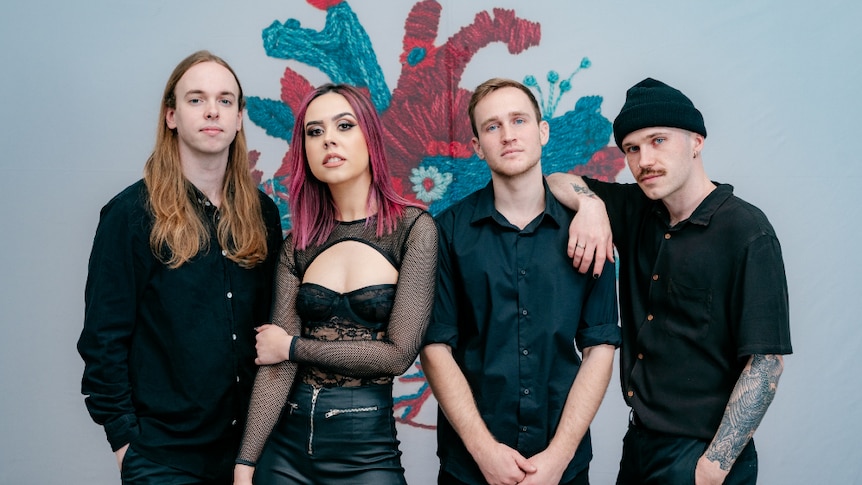 Press image of Yours Truly; members dressed in black against blue wall