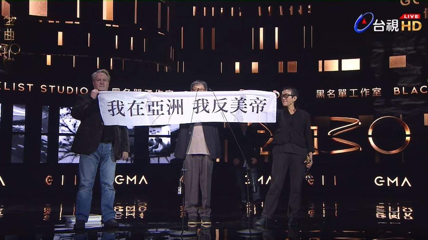 Three people on stage hold a banner with Chinese text.