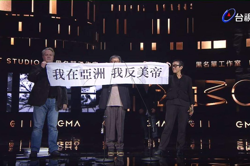 Three people on stage hold a banner with Chinese text.