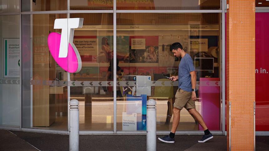 Un hombre pasa junto a una tienda Telstra en Darwin y mira su teléfono.