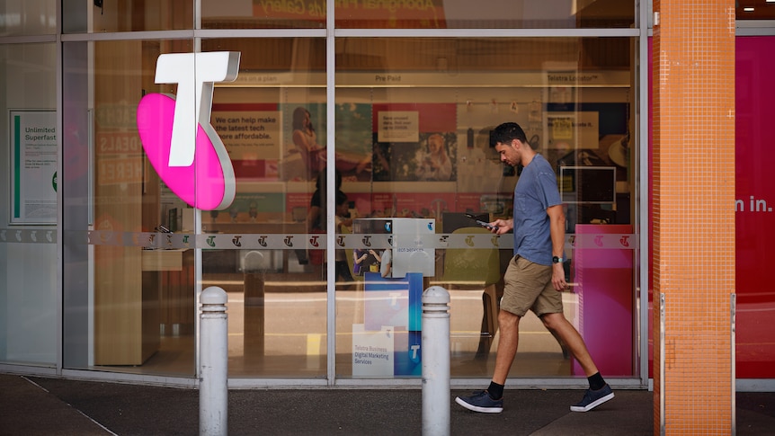 A man walks past a Telstra shop in Darwin, he looks down at his phone.