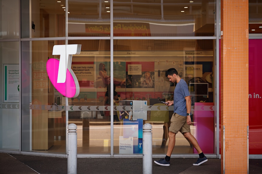 A man walks past a Telstra shop in Darwin, he looks down at his phone.