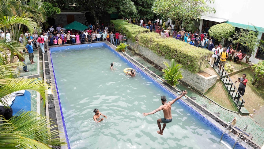 People stand around a pool as few others jump in to swim in the president's pool.