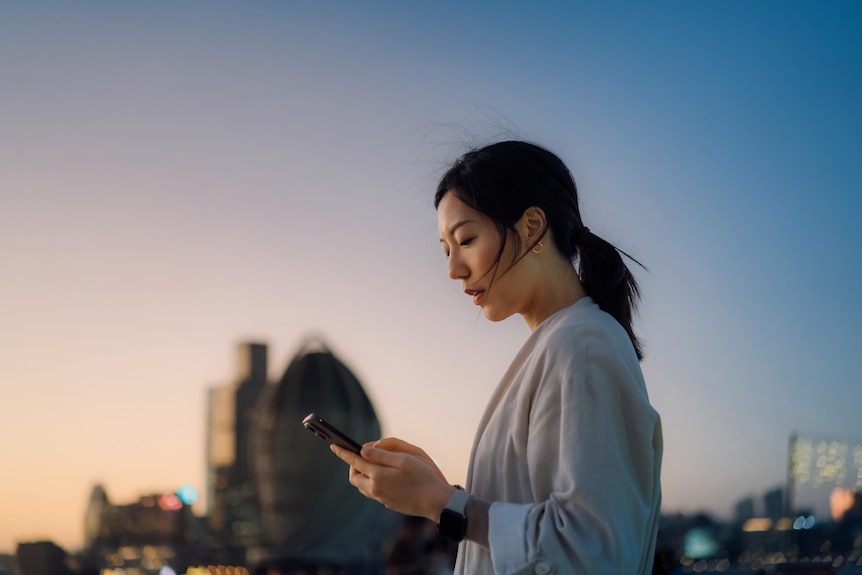 A young Asian woman is pictured walking in the city while looking at her phone