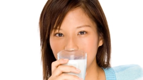 A woman holding a glass of milk to her lips.