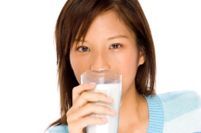 A woman holding a glass of milk to her lips.
