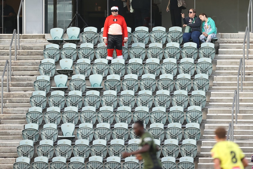 A man wearing a red outfit stands in empty seats during a soccer game