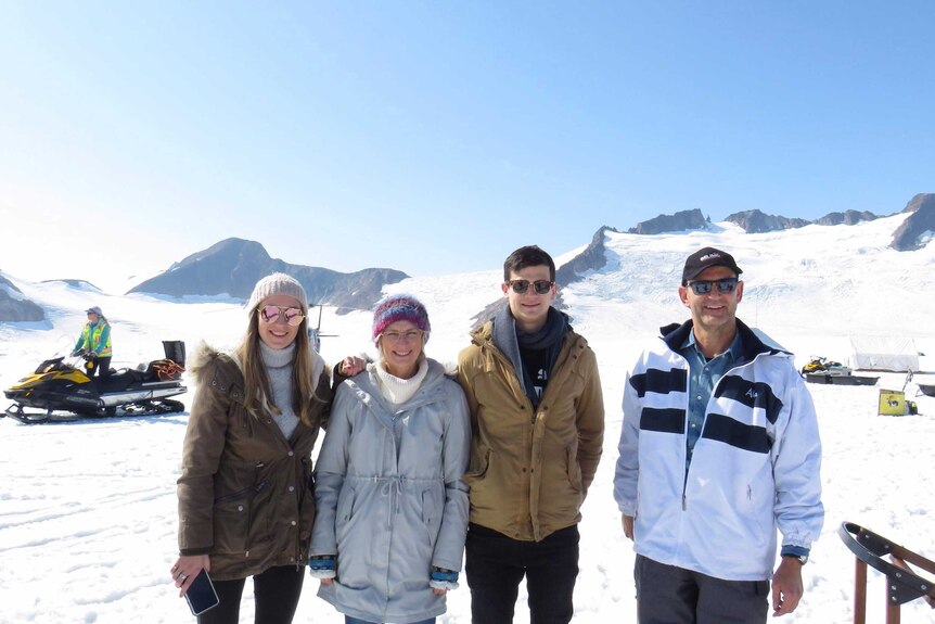 Four people stand in a line on a glacier.