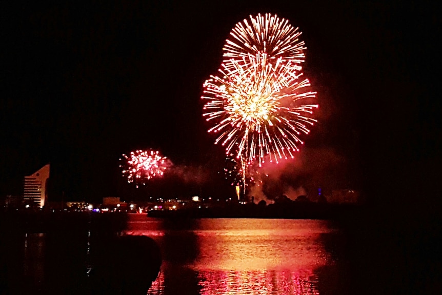 Fireworks at night reflect over a lake