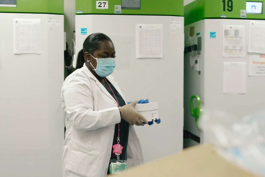 A lab technician holds a box of vaccines near a cold storage unit