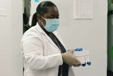A lab technician holds a box of vaccines near a cold storage unit