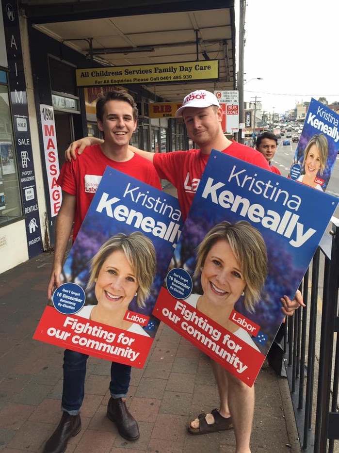 Two young men in Labor T-shirts hold up capaign posters with Kristina Keneally's face on them.