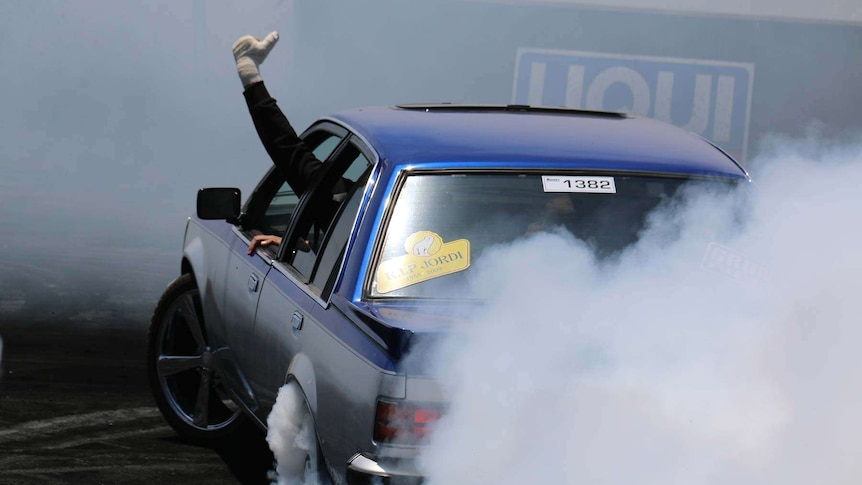 A passenger waves to the crowd mid-burnout at Summernats.
