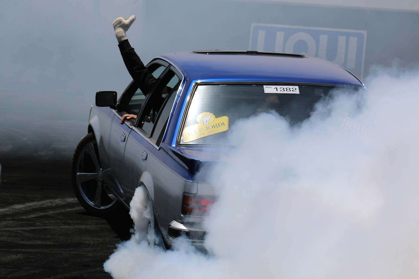 A passenger waves to the crowd mid-burnout at Summernats.