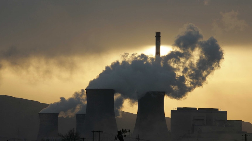 A coal fired power plant covered in smoke and the sun behind it