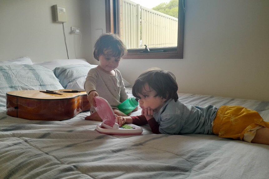 Two kids playing on a bed.