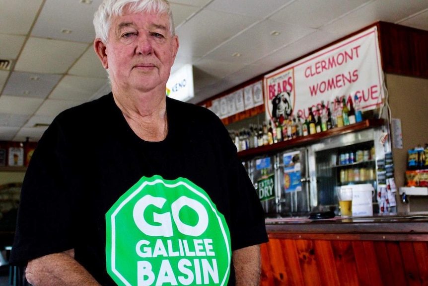 Clermont publican Les Boal stands beside the bar of his pub in a a green 'Go Galilee Basin' t-shirt.