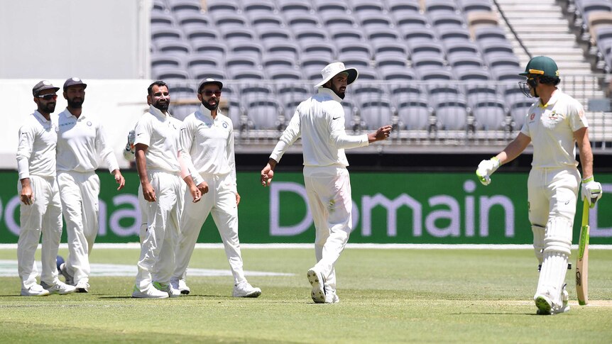 A man wearing batting gear turns his head towards a group of fielders who are all looking in his direction