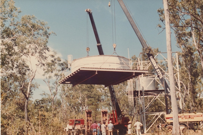 An old photo of a large tank being lifted by a crane.