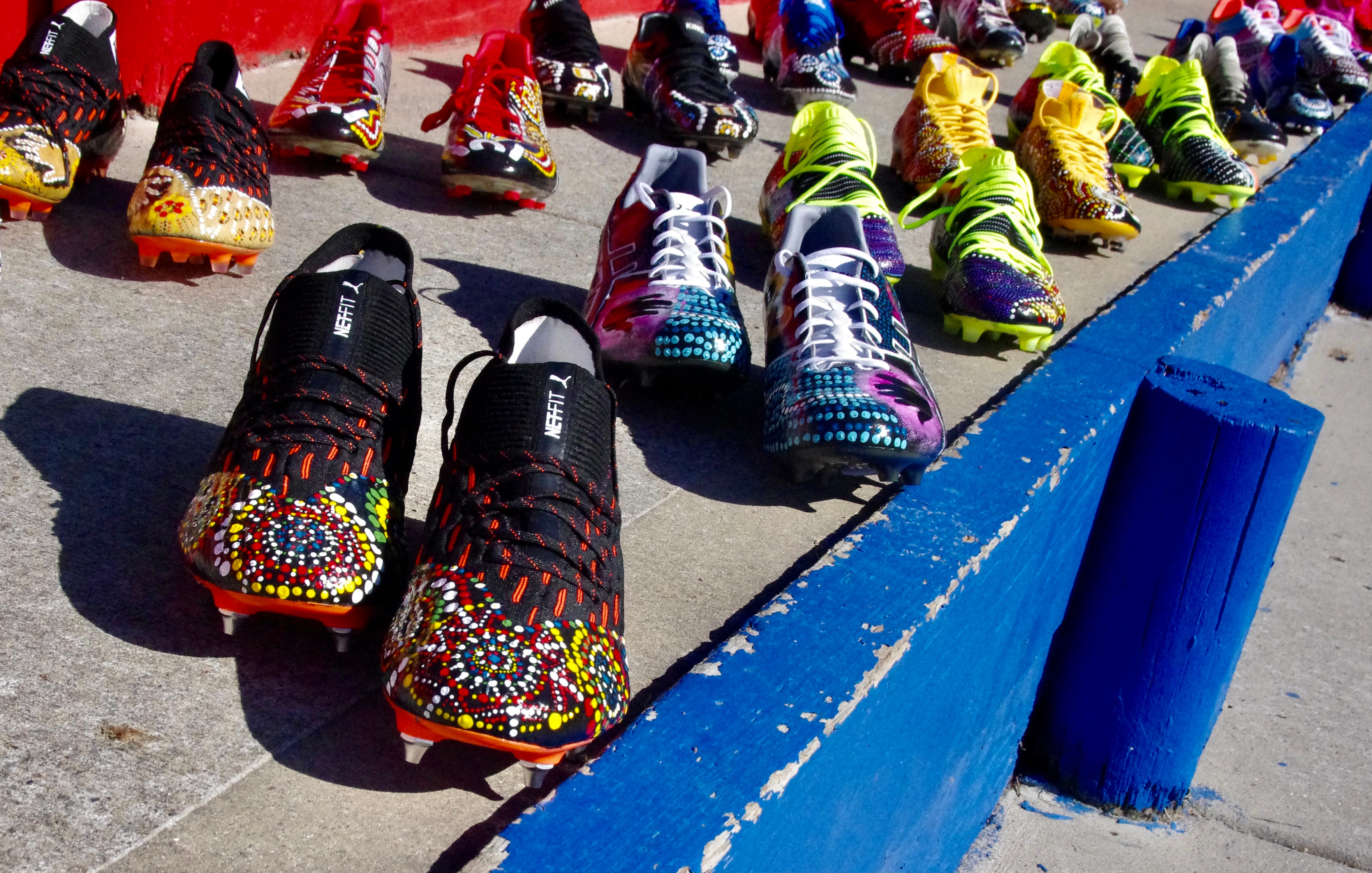 Multiple pairs of football boots with Indigenous artwork lined up.