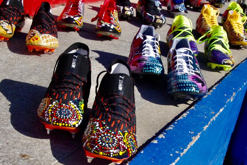 Multiple pairs of football boots with Indigenous artwork lined up.