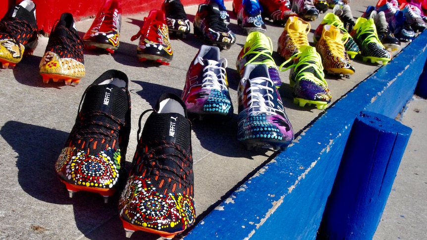 Multiple pairs of football boots with Indigenous artwork lined up.