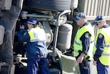 Three police officers examine the underside of a bus that has turned on its side.