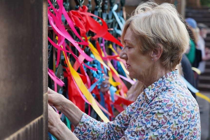 A woman ties a ribbon to a fence covered in them
