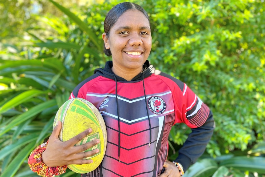 Wanita remaja Aborigin memegang bola dan tersenyum