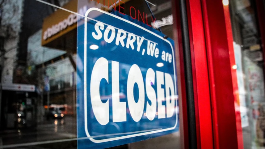 Sorry we are closed sign hangs in the window of a storefront.