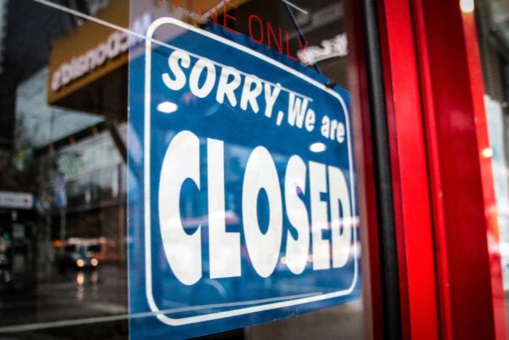 Sorry we are closed sign hangs in the window of a storefront.