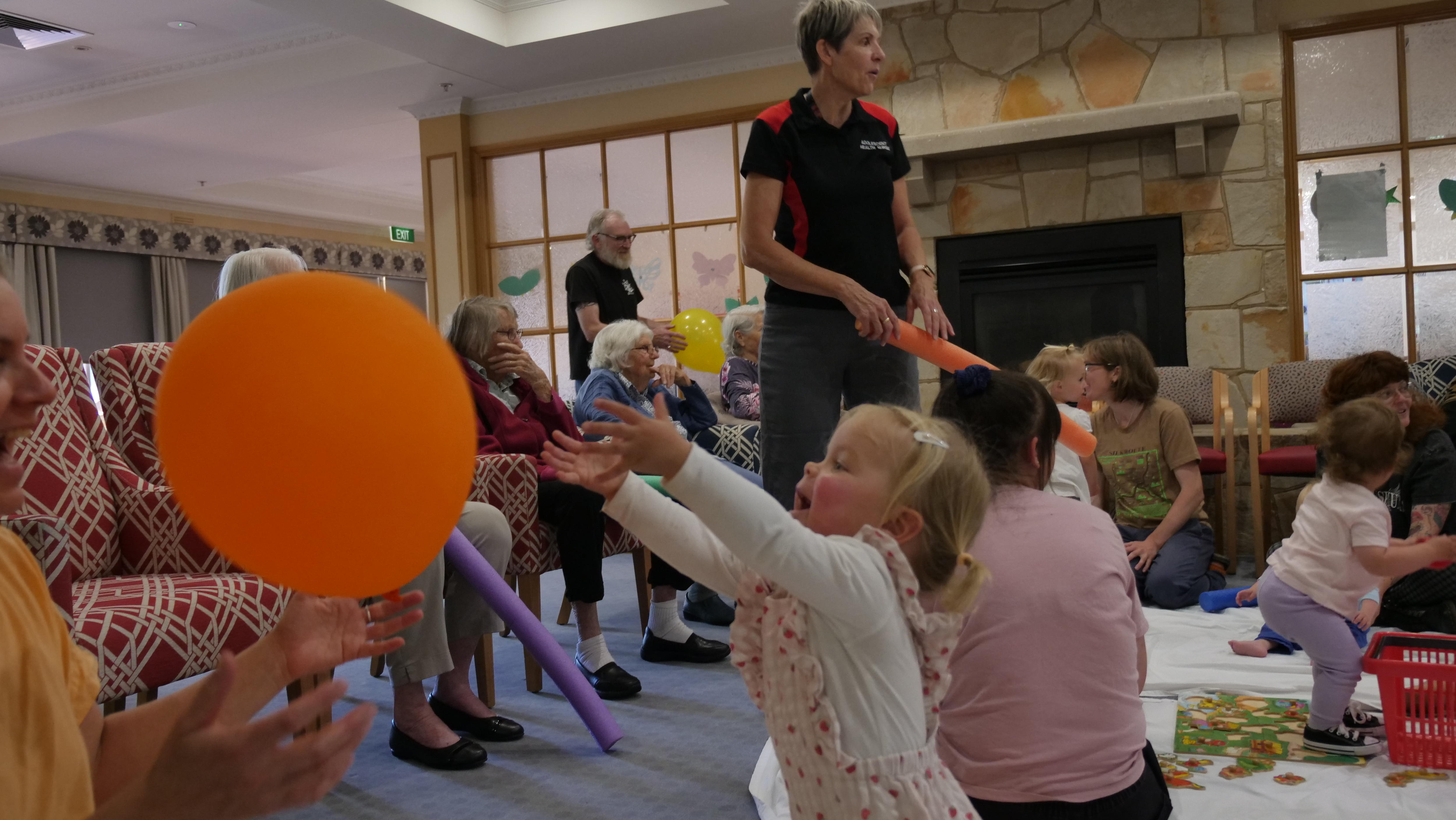a toddler in frilly overalls reaches for an inflated orange balloon
