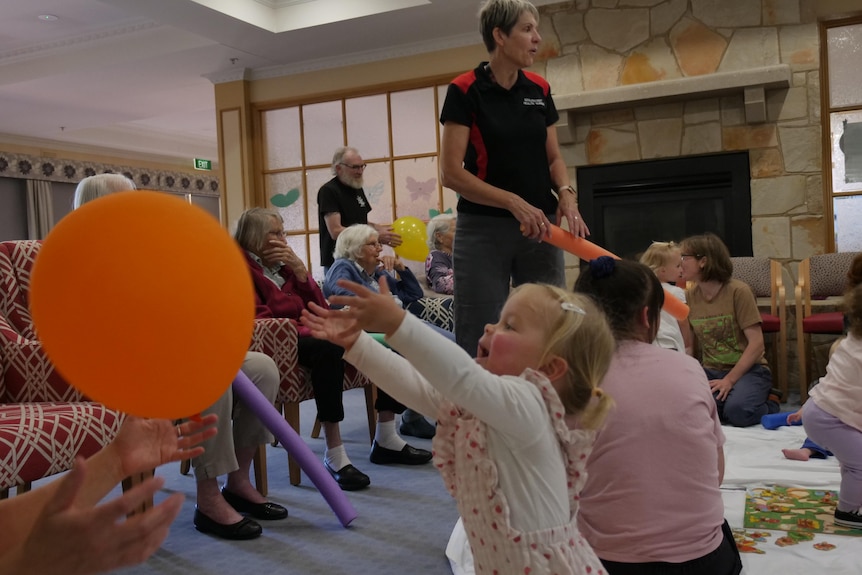 a toddler in frilly overalls reaches for an inflated orange balloon
