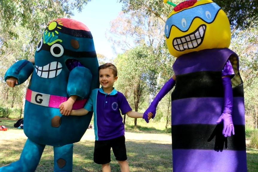 A boy holds hands with people who are wearing colourful costumes