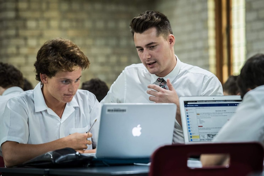 Austin Ward (right) a teaching school student is seen at a desk speaking to a year 10 student from St Philip's Christian College