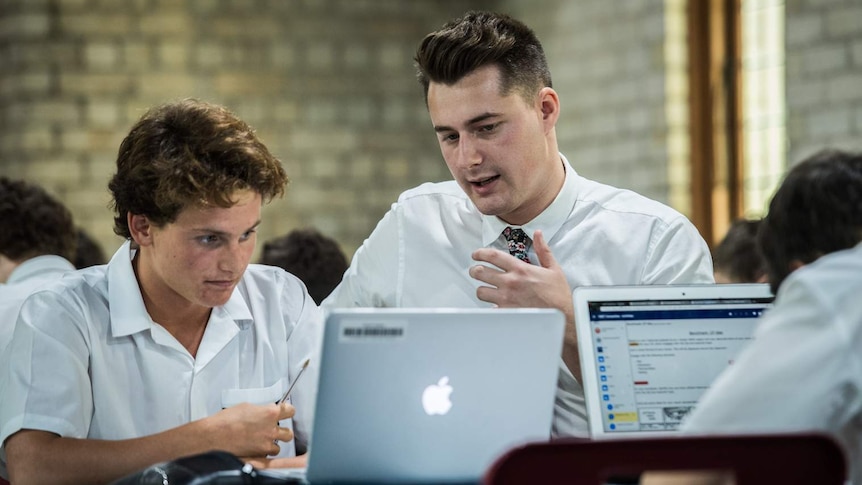 Austin Ward (right) a teaching school student is seen at a desk speaking to a year 10 student from St Philip's Christian College