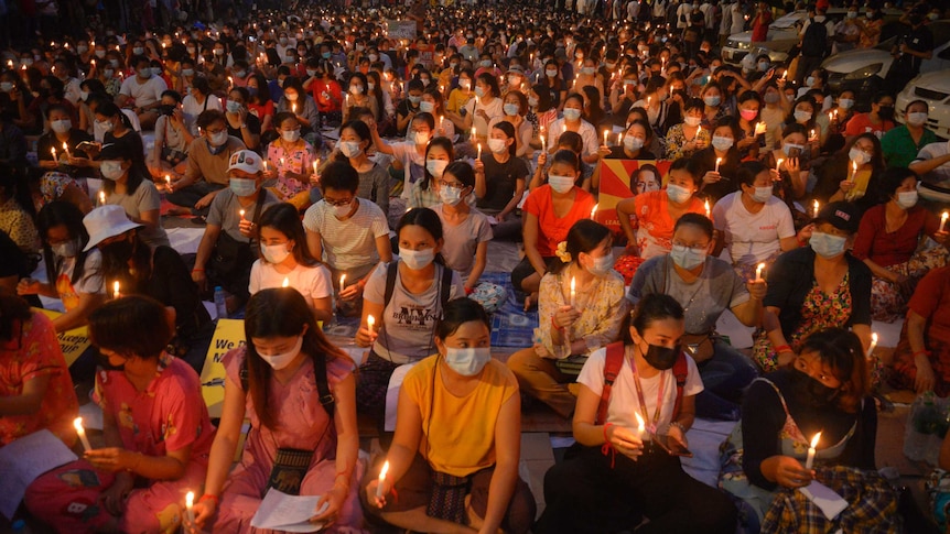 A huge group of sitting protesters, many wearing face masks, raise candles in their hands.