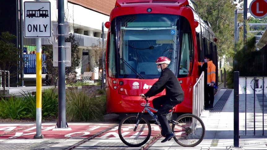 A man rides a bicycle near the Newcastle light rail tram.