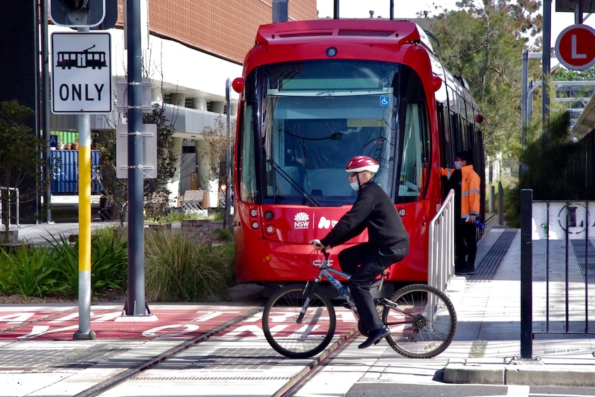 A man rides a bicycle near the Newcastle light rail tram.
