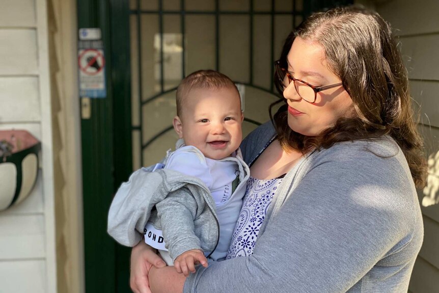 A woman looks at the baby boy she is holding, who is smiling at the camera.