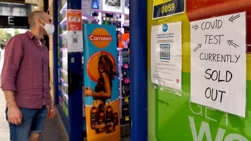 A man looking inside a chemist, with a sign saying no covid tests.