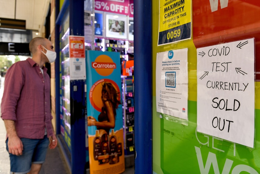 A man looking inside a chemist, with a sign saying no covid tests.