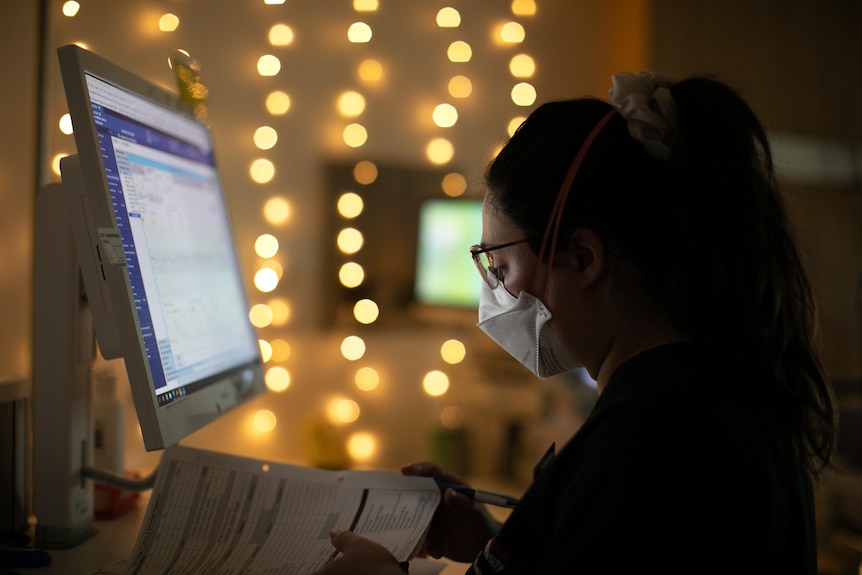 Bella in a dimly-lit materinty suite, standing near a computer monitor and leafing through paperwork.