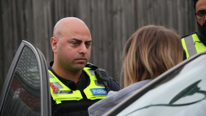 A male police officer speaks with a woman near her car.