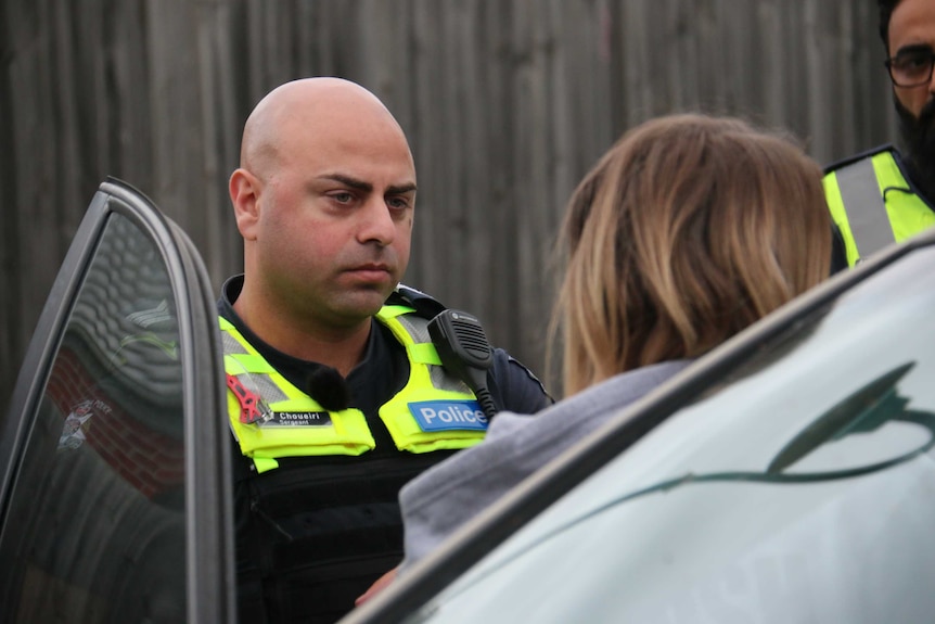 A male police officer speaks with a woman near her car.