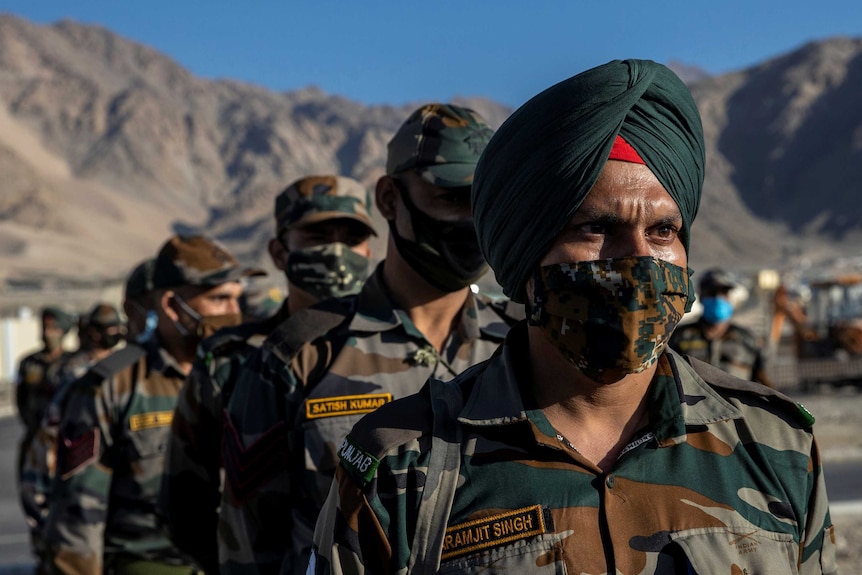 Indian soldiers stand in a formation after disembarking from a military transport plane.