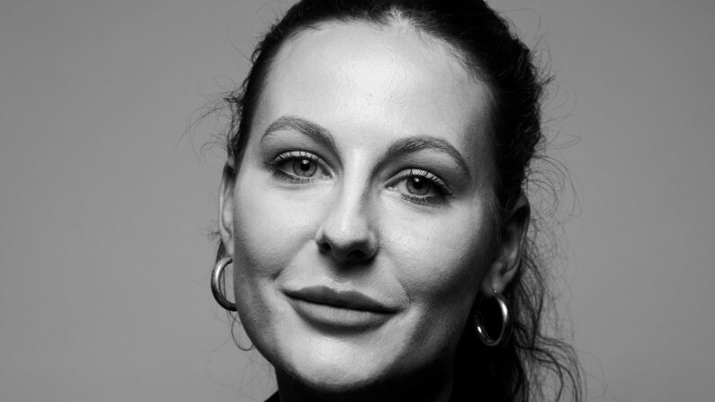 Black and white photo of a younger white woman. Long hair is pulled back from her face into a ponytail