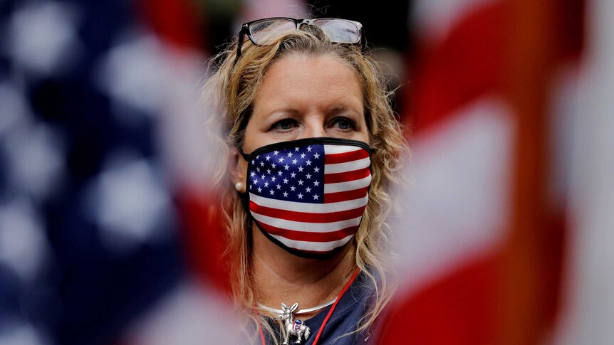 A woman in a US flag face mask stands between two American flags