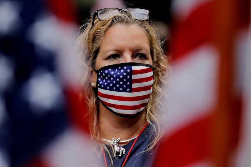 A woman in a US flag face mask stands between two American flags