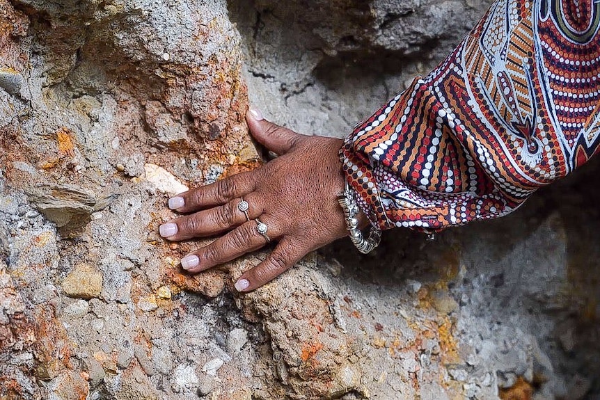 A woman's hand with jewellery placed on the side of a rock. 